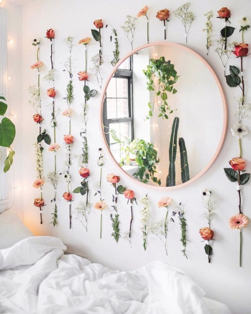 Roses and baby's breath flowers hung on the wall around a circular mirror in an aesthetic room